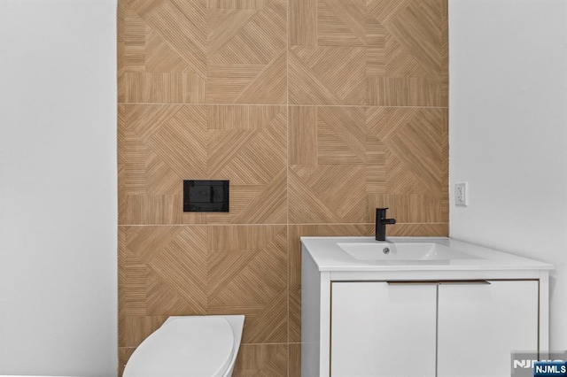 bathroom featuring vanity, tile walls, and toilet