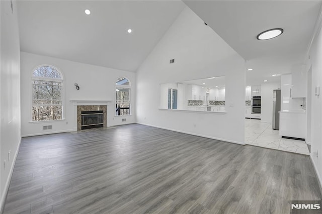 unfurnished living room featuring light hardwood / wood-style floors, high vaulted ceiling, and a premium fireplace