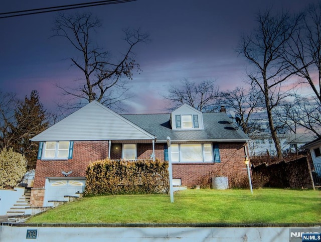 cape cod-style house with an attached garage, a front yard, stairway, and brick siding