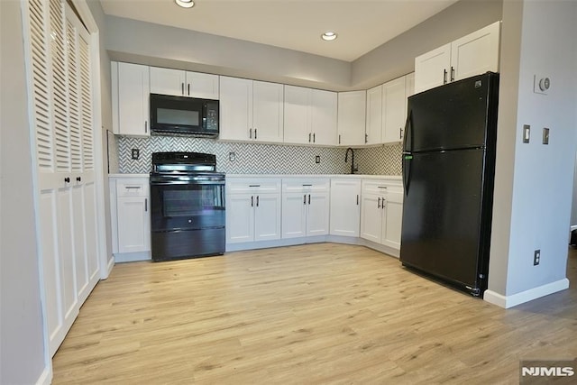 kitchen with white cabinetry, light hardwood / wood-style flooring, backsplash, and black appliances