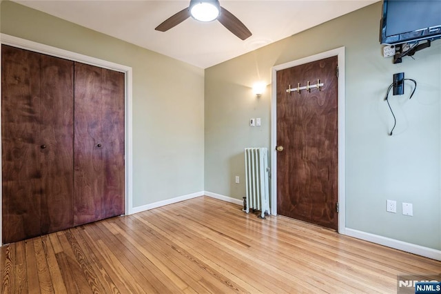 unfurnished bedroom featuring ceiling fan, radiator heating unit, and light wood-type flooring