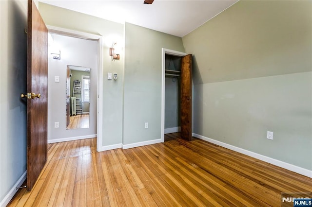 unfurnished bedroom featuring lofted ceiling, a closet, and light wood-type flooring