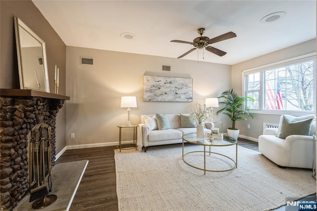 living room with dark wood-type flooring, ceiling fan, and a stone fireplace