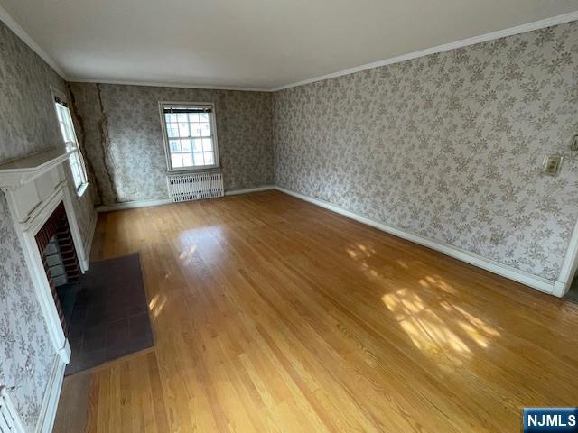 unfurnished living room featuring wallpapered walls, baseboards, ornamental molding, wood finished floors, and a fireplace