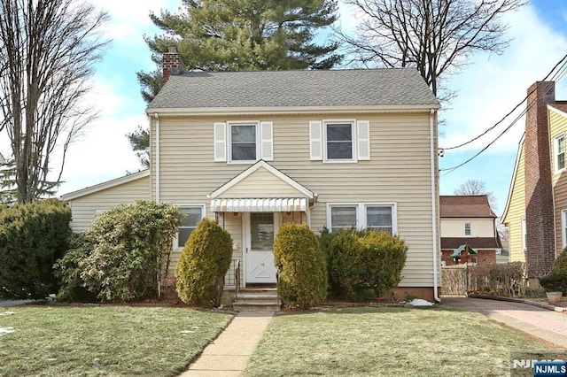 view of front facade featuring entry steps, roof with shingles, a chimney, and a front lawn