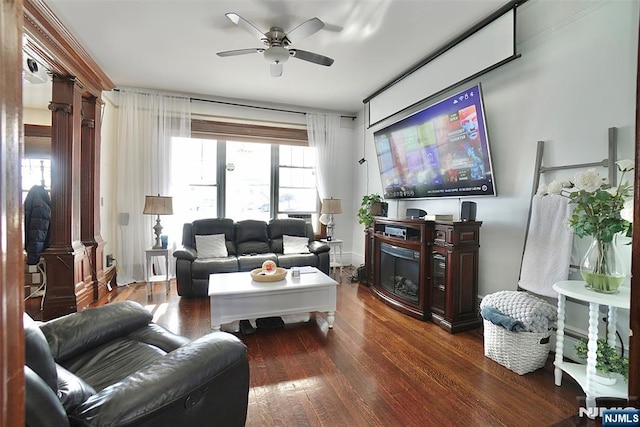 living room with decorative columns, dark wood-type flooring, and ceiling fan