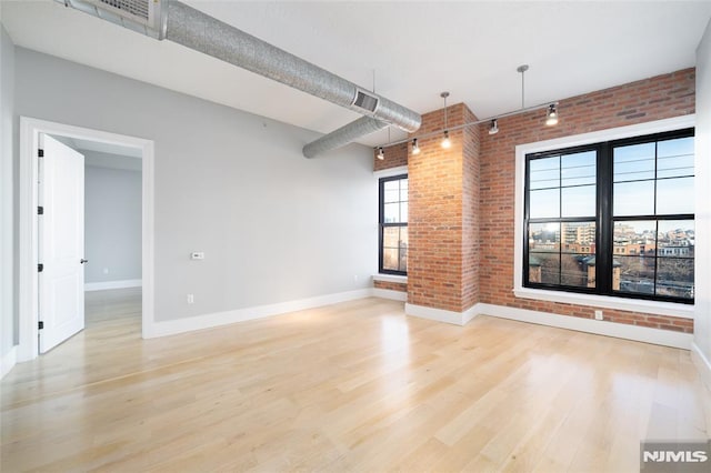 unfurnished living room featuring track lighting, brick wall, and light wood-type flooring