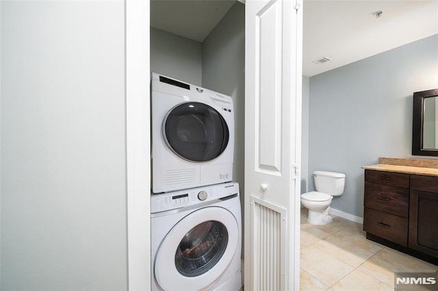 laundry area with stacked washer and clothes dryer and light tile patterned floors