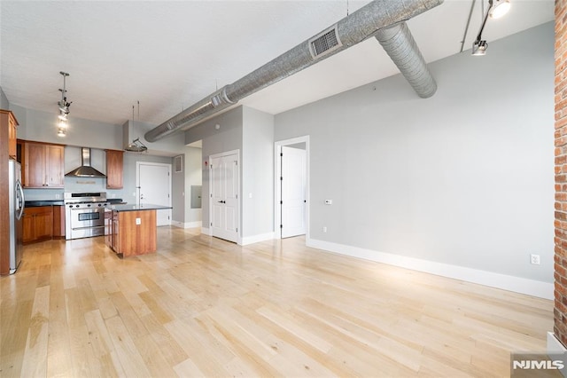 kitchen with hanging light fixtures, stainless steel appliances, light hardwood / wood-style floors, a kitchen island, and wall chimney exhaust hood