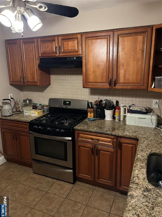 kitchen featuring light stone counters, light tile patterned floors, decorative backsplash, and stainless steel gas range oven