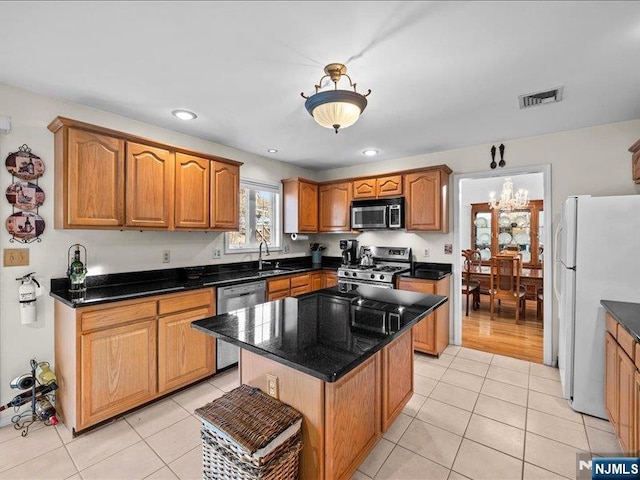 kitchen with sink, appliances with stainless steel finishes, a notable chandelier, a kitchen island, and light tile patterned flooring