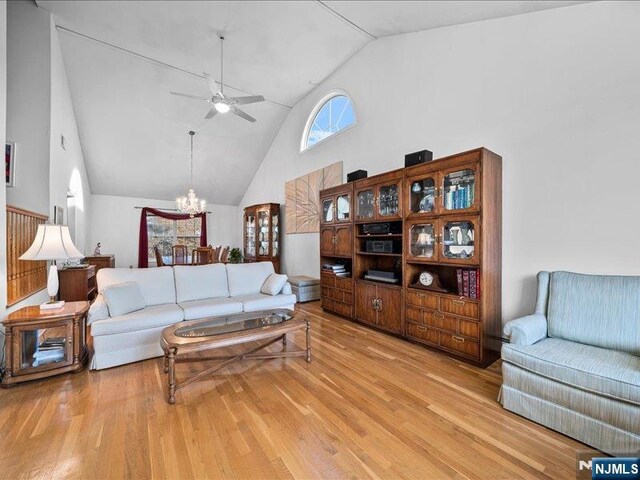 living room with hardwood / wood-style floors, ceiling fan with notable chandelier, and high vaulted ceiling