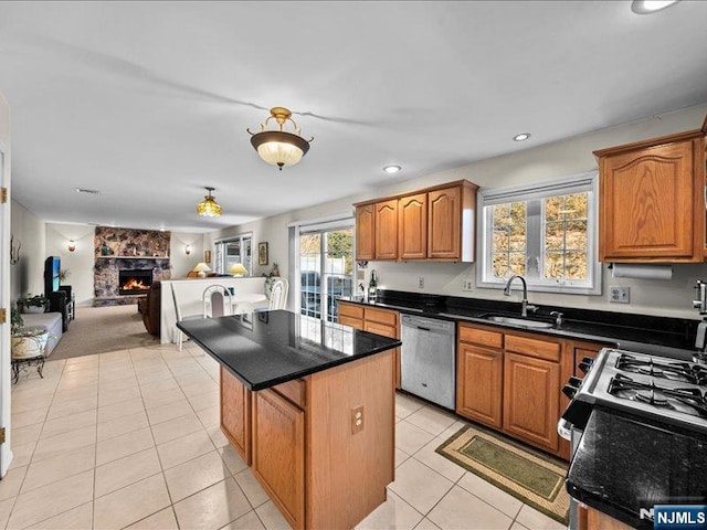 kitchen with sink, light tile patterned floors, stainless steel dishwasher, a kitchen island, and a fireplace