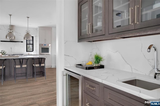 bar with wine cooler, sink, hanging light fixtures, oven, and light stone countertops