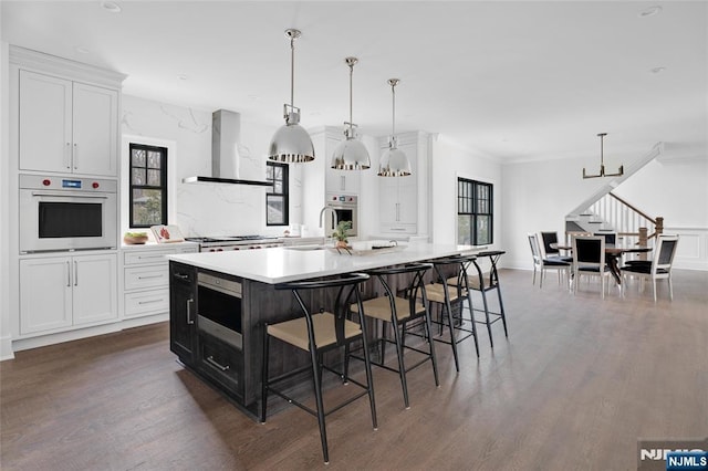 kitchen featuring stainless steel appliances, hanging light fixtures, a large island, and wall chimney range hood