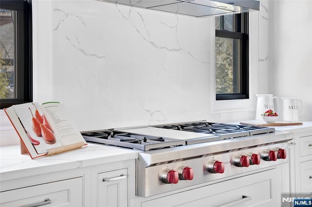 kitchen featuring white cabinetry, stainless steel gas stovetop, light stone countertops, and extractor fan