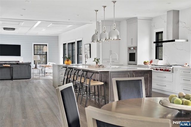 kitchen featuring pendant lighting, a breakfast bar area, white cabinets, oven, and a center island with sink