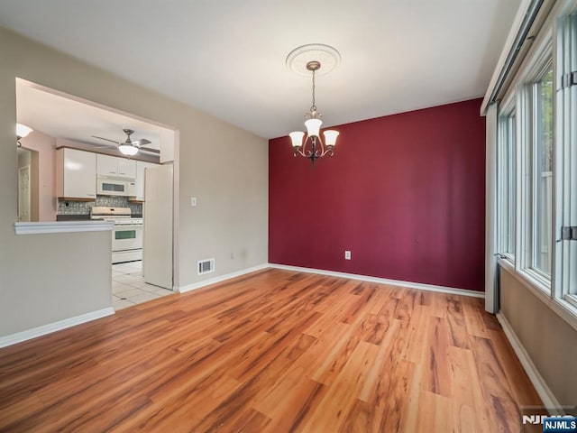 unfurnished dining area with ceiling fan with notable chandelier and light wood-type flooring