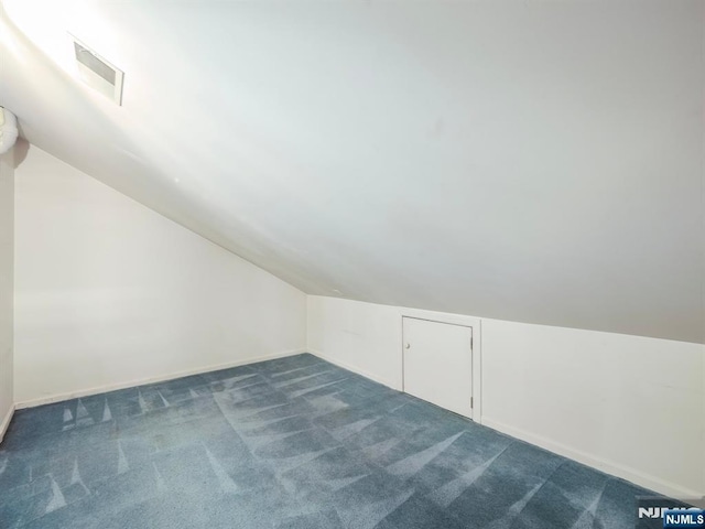 bonus room with dark colored carpet and lofted ceiling