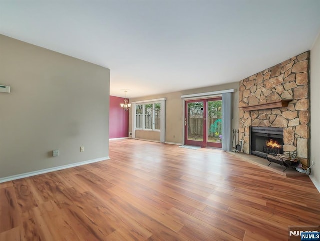 unfurnished living room with an inviting chandelier, a stone fireplace, and light wood-type flooring