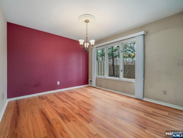 empty room featuring wood-type flooring and an inviting chandelier