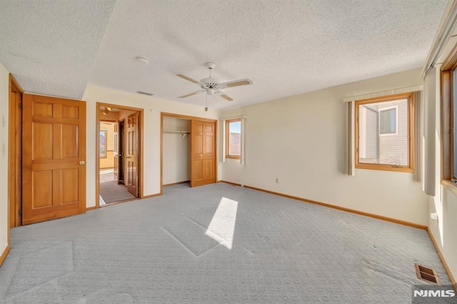 unfurnished bedroom with ceiling fan, light colored carpet, a closet, and a textured ceiling