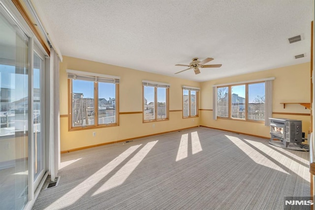 unfurnished living room featuring ceiling fan, a textured ceiling, light carpet, and a wood stove