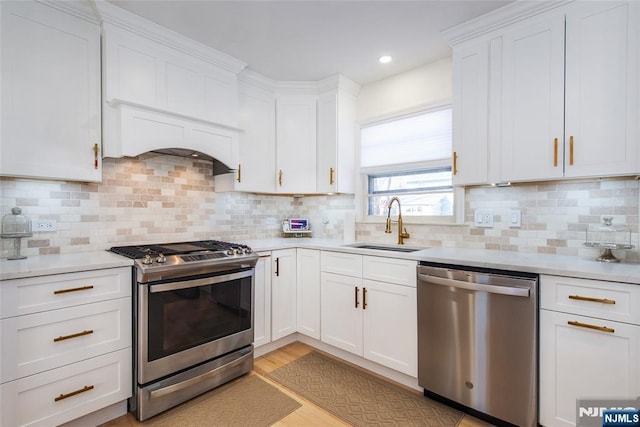 kitchen with sink, light hardwood / wood-style flooring, appliances with stainless steel finishes, white cabinetry, and tasteful backsplash