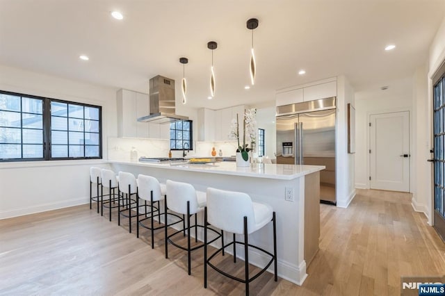 kitchen featuring built in refrigerator, decorative light fixtures, kitchen peninsula, range hood, and white cabinets