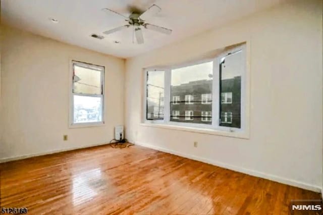 empty room featuring a ceiling fan, visible vents, baseboards, and wood finished floors