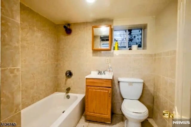 bathroom with shower / tub combination, toilet, tile patterned flooring, vanity, and tile walls