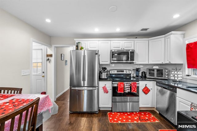 kitchen with tasteful backsplash, appliances with stainless steel finishes, white cabinets, and dark hardwood / wood-style flooring