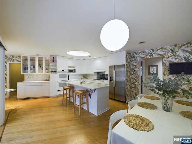 kitchen featuring wallpapered walls, appliances with stainless steel finishes, decorative light fixtures, light countertops, and white cabinetry