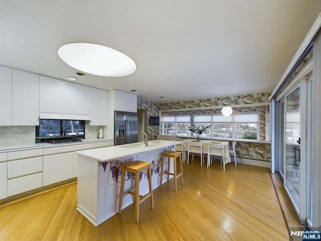 kitchen with a center island with sink, light countertops, white cabinetry, stainless steel fridge, and wallpapered walls