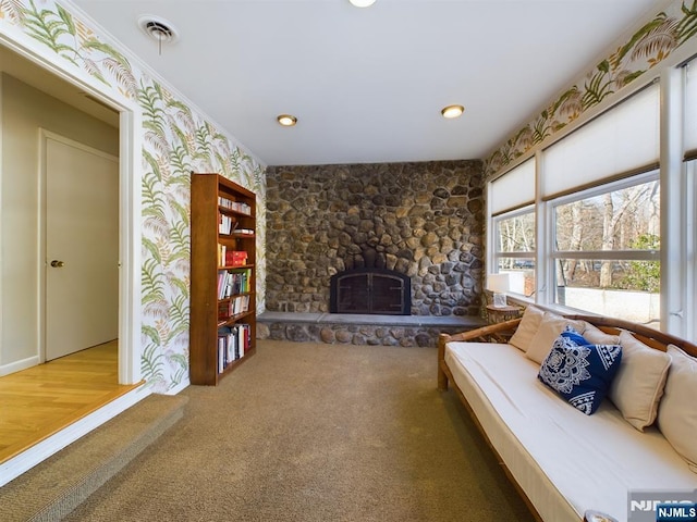 unfurnished living room with wallpapered walls, visible vents, ornamental molding, and a stone fireplace