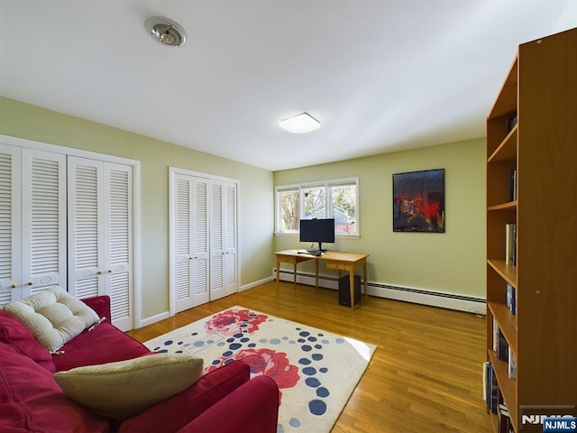 interior space with a baseboard heating unit, light wood finished floors, and baseboards