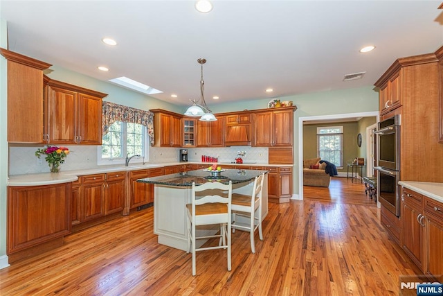 kitchen with a kitchen bar, a skylight, dark stone countertops, a kitchen island, and stainless steel double oven