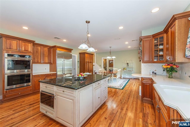 kitchen featuring hanging light fixtures, white cabinetry, built in appliances, and light hardwood / wood-style floors