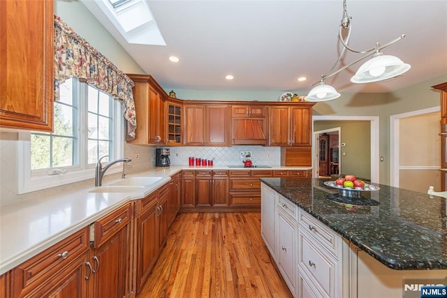 kitchen featuring pendant lighting, a skylight, sink, dark stone counters, and light hardwood / wood-style flooring