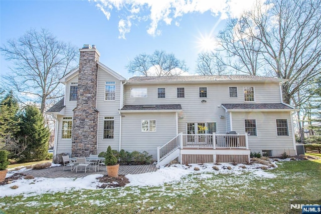 snow covered back of property with central AC unit, a patio area, a deck, and a lawn