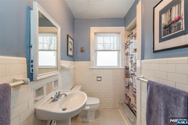 bathroom featuring plenty of natural light, toilet, sink, and tile walls