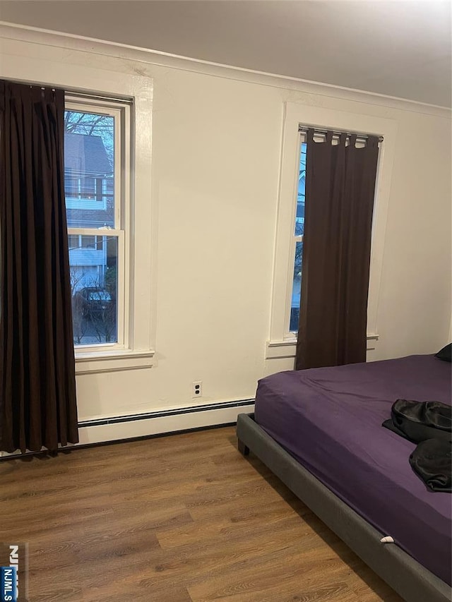 bedroom with a baseboard radiator, wood-type flooring, and ornamental molding