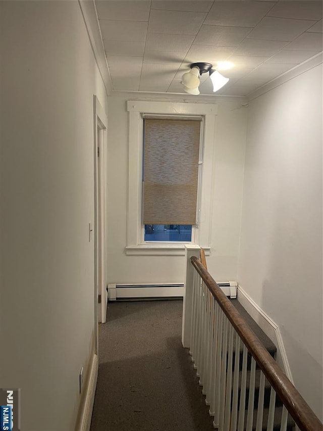 corridor with a baseboard radiator, ornamental molding, and dark carpet