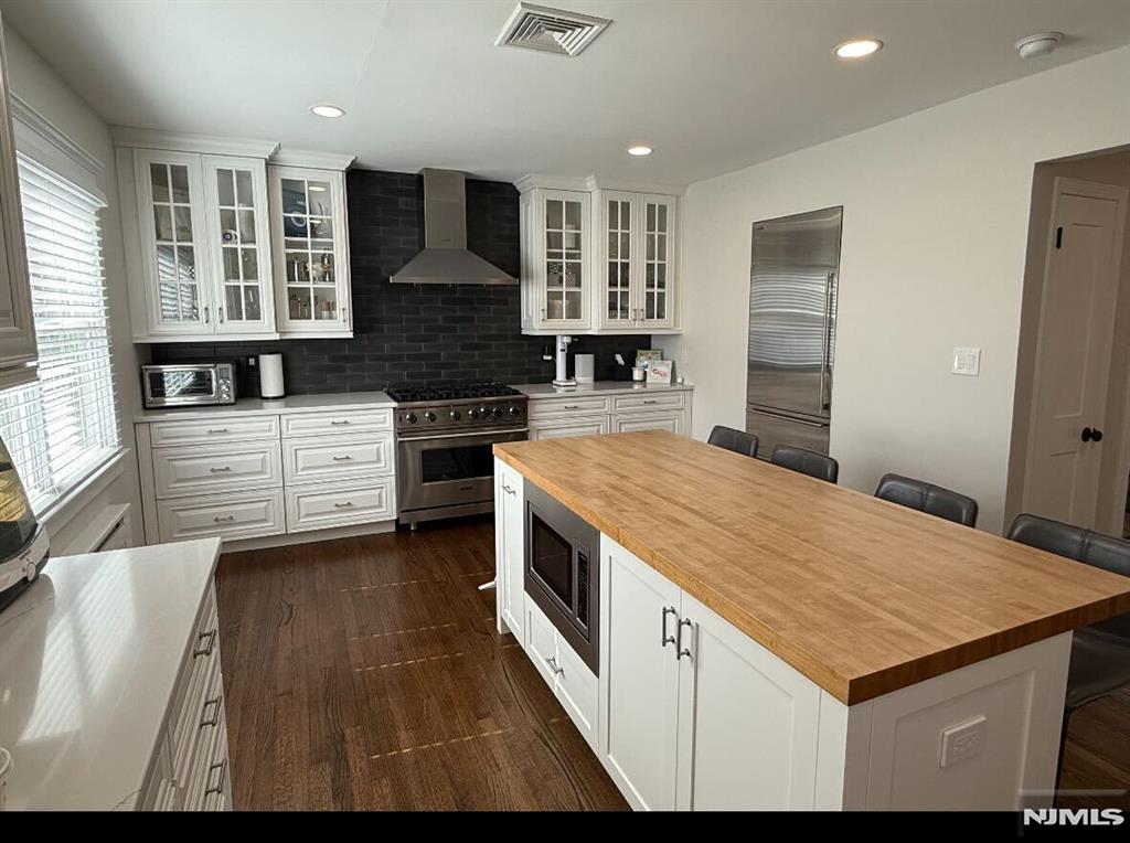 kitchen featuring white cabinetry, appliances with stainless steel finishes, a center island, and wall chimney exhaust hood