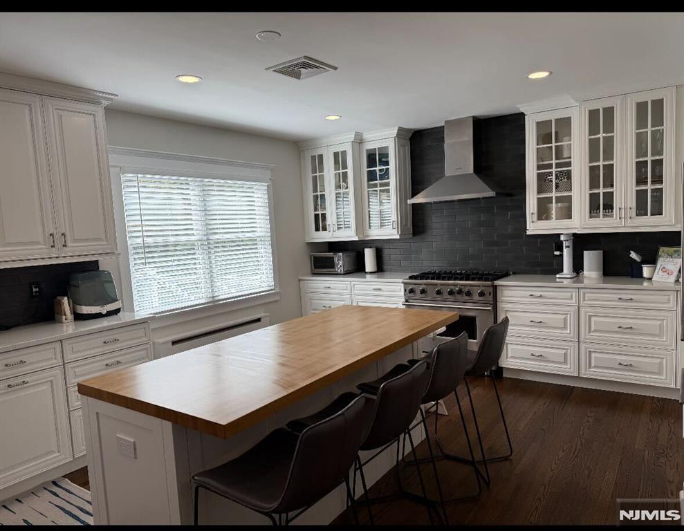 kitchen featuring white cabinetry, high end range, wall chimney exhaust hood, and a center island