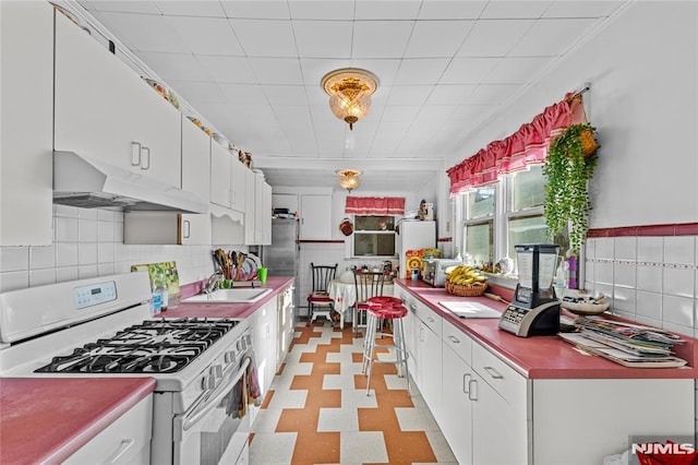 kitchen featuring tasteful backsplash, sink, white range with gas stovetop, and white cabinets