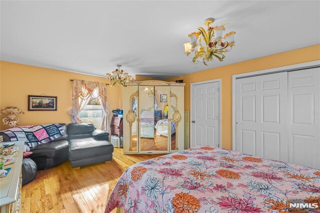 bedroom with a notable chandelier, hardwood / wood-style flooring, and multiple closets