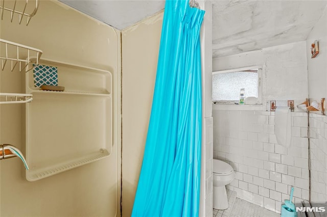 bathroom with tile patterned floors, toilet, curtained shower, and tile walls