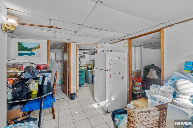 basement with white refrigerator, light tile patterned flooring, and a paneled ceiling