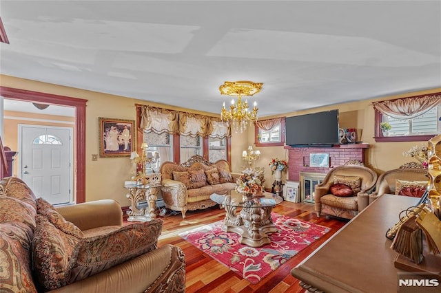 living room featuring an inviting chandelier, hardwood / wood-style floors, and a brick fireplace